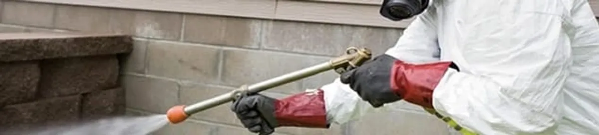 Pest control technician applying exterior insect treatment along a home foundation in Allentown, PA