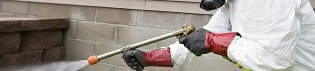 Pest control technician applying exterior insect treatment along a home foundation in Allentown, PA
