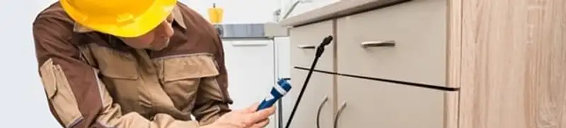 Roach exterminator applying treatment under kitchen cabinets in Allentown, PA