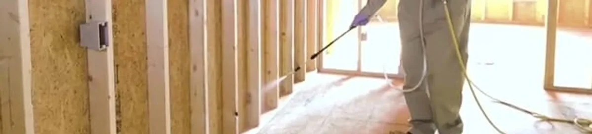 Termite treatment technician applying spray along framing and unfinished walls in Allentown, PA