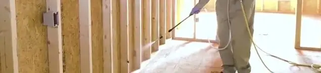 Termite treatment technician applying spray along framing and unfinished walls in Allentown, PA
